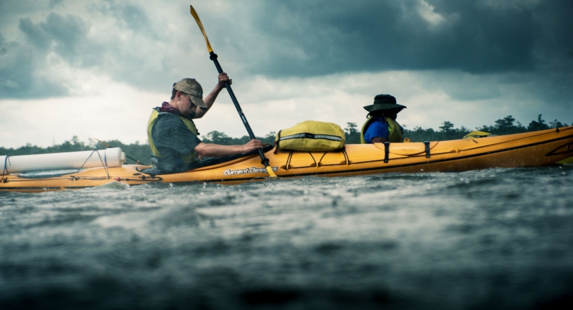 a young person works to paddle a kayak while it rains